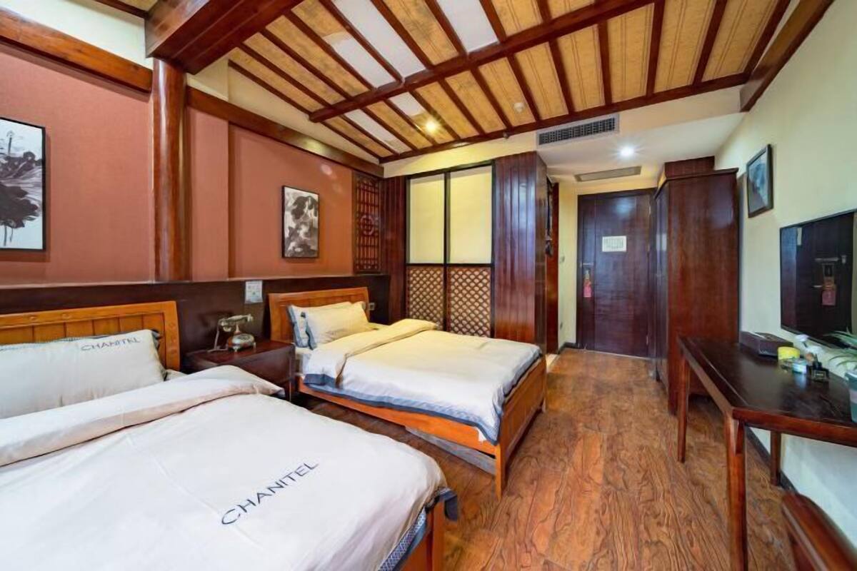 A hotel room with two beds, wooden flooring, a TV, and a wardrobe.
