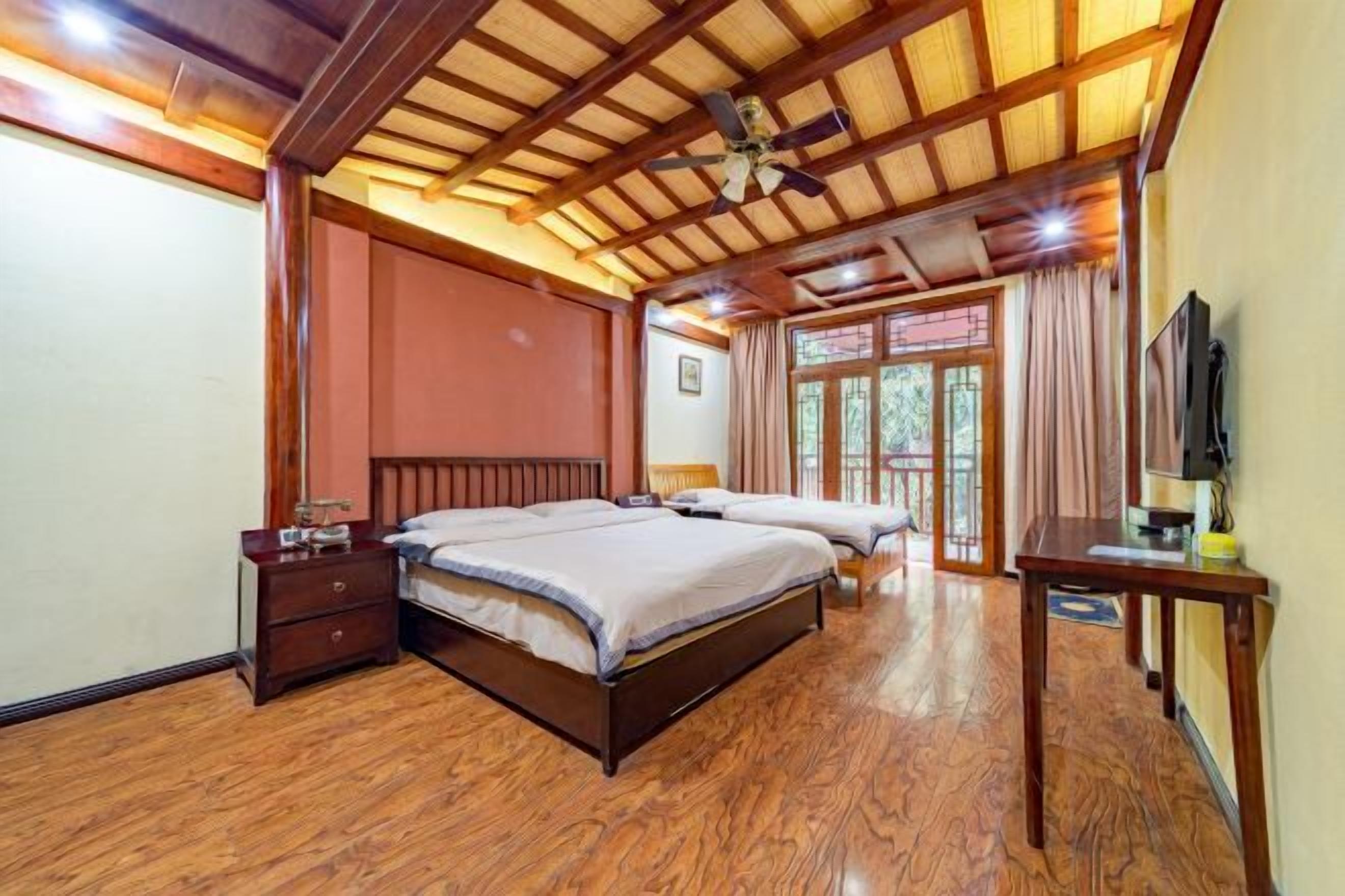 Quarto com teto de madeira, duas camas, mesa de cabeceira, televisão e janela com cortinas.