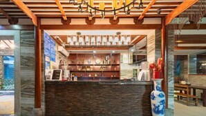 A reception area with a stone counter, wooden beams, and a large vase. - Yangshuo wanglai Hotels (Yangshuo)