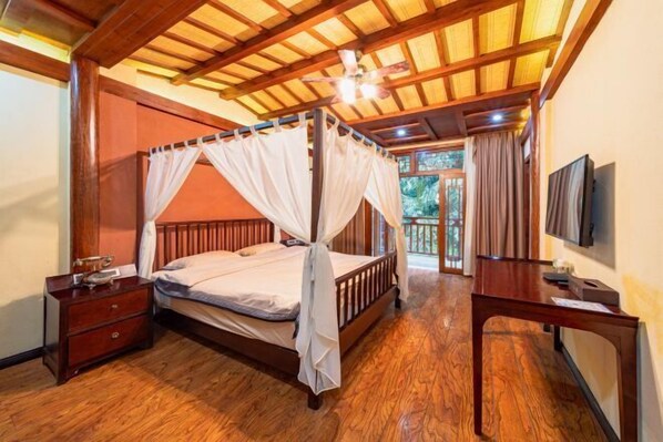 A four-poster bed with a canopy, a wooden nightstand, a desk with a chair, and a television on the wall.