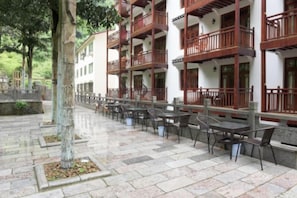 An outdoor seating area with tables and chairs, a tree, and a building with balconies. - Yangshuo wanglai Hotels (Yangshuo)