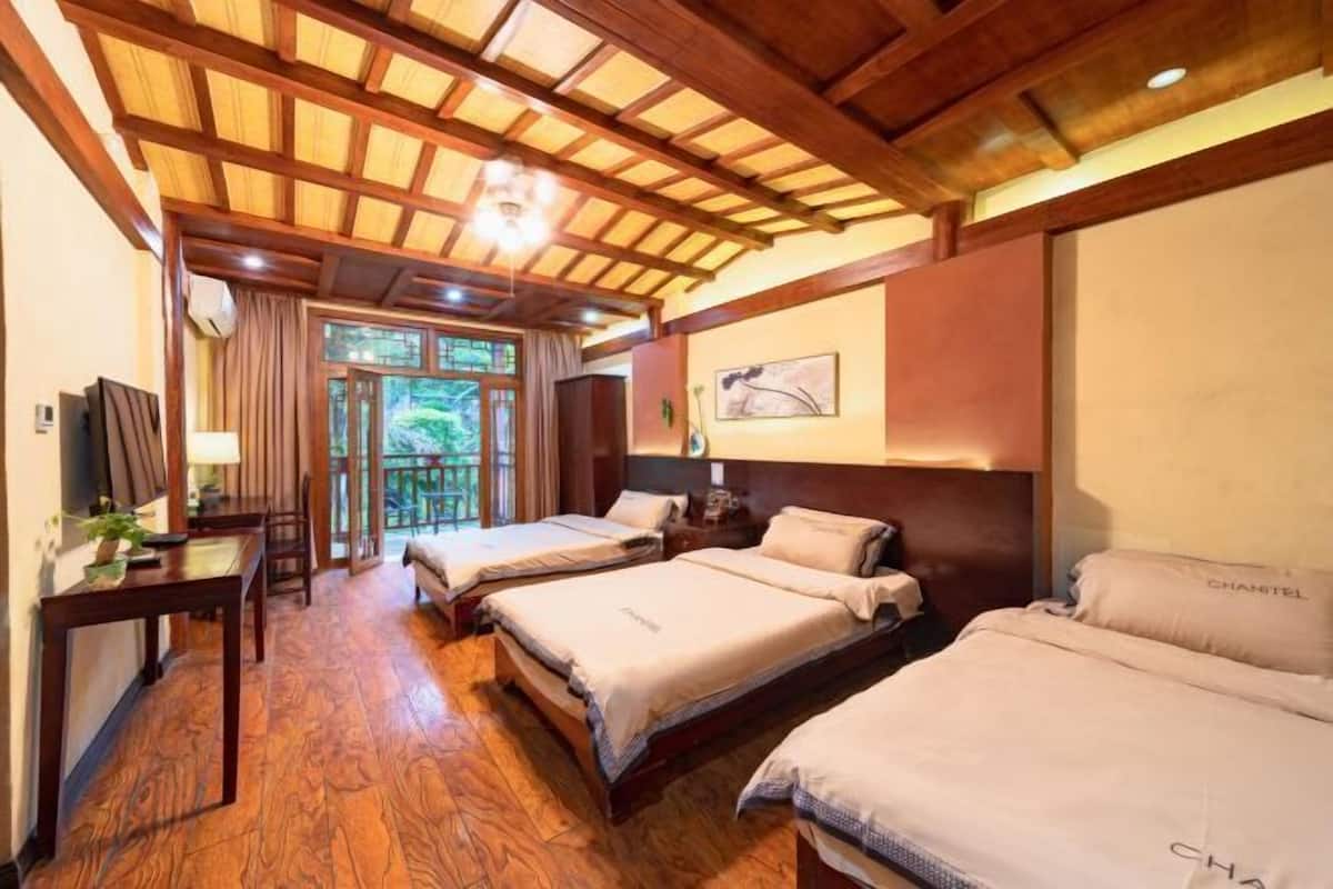 A hotel room with wooden flooring, a large bed, a smaller bed, a desk with a lamp, and a view through a glass door.