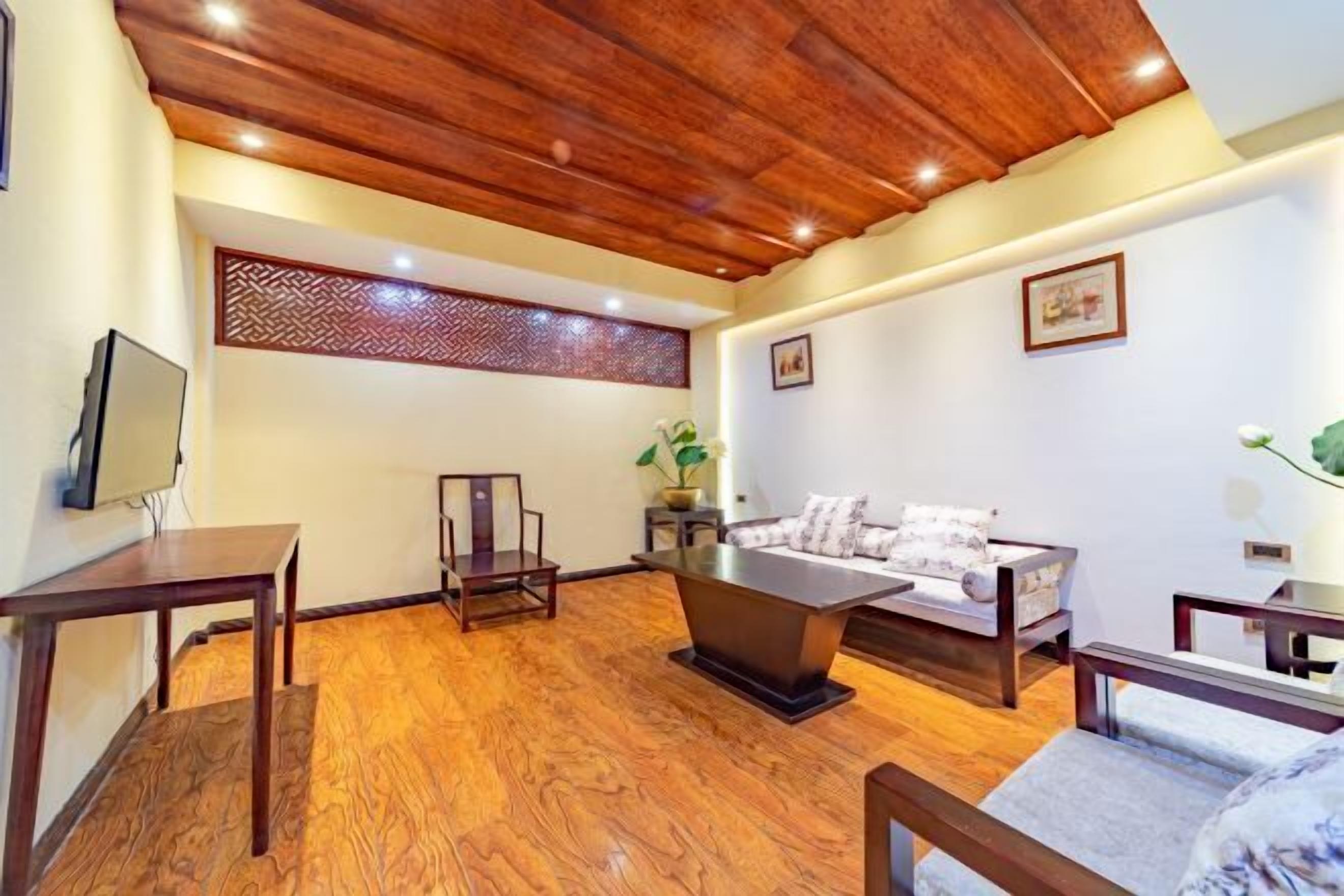 Quarto com teto de madeira, sofá, mesa de centro, TV e um painel decorativo na parede.