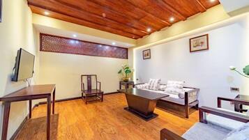 Quarto com teto de madeira, sofá, mesa de centro, TV e um painel decorativo na parede.