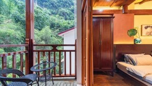 A balcony with a wooden railing, a small table, two wicker chairs, and a view of a forested area. - Yangshuo wanglai Hotels (Yangshuo)