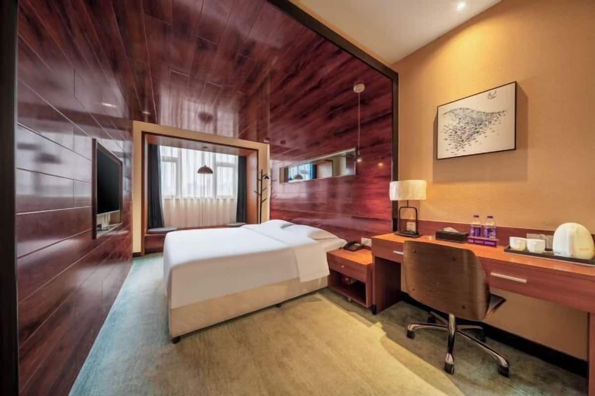 Une chambre d’hôtel avec un plafond en bois, un lit, un bureau, une chaise, un téléviseur et une œuvre d’art encadrée au mur.