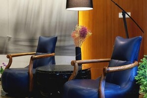 Una habitación con dos sillones de cuero azul, una mesita redonda, una lámpara y un jarrón con flores.
