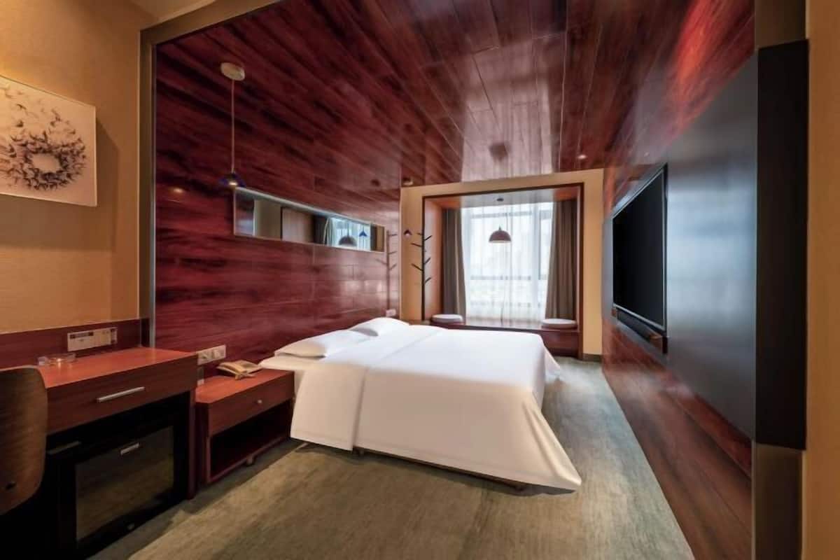 Une chambre d’hôtel avec un plafond en bois, un lit, un bureau, une télévision et une fenêtre.