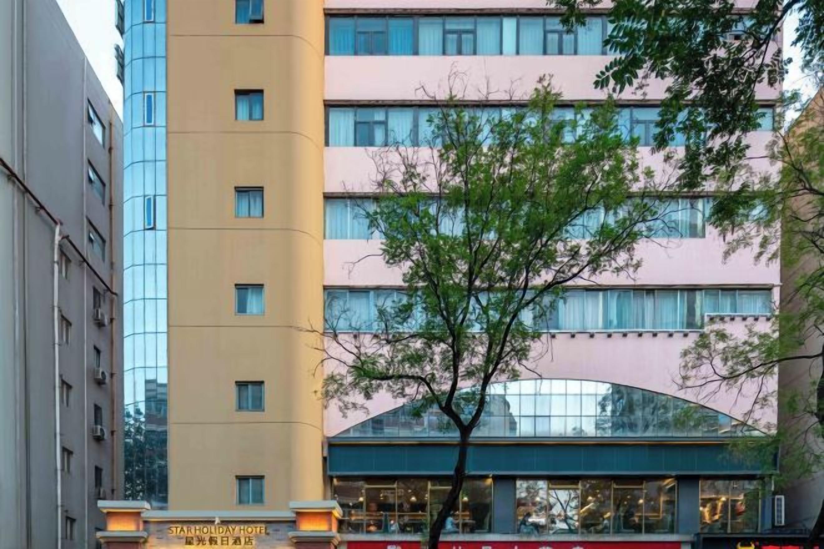 A multi-story hotel building with a modern facade, a visible entrance, and a tree in front.