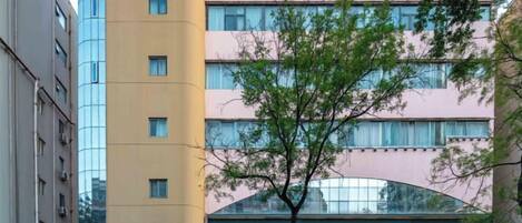 A multi-story hotel building with a modern facade, a visible entrance, and a tree in front.