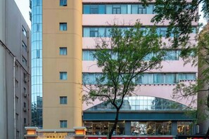 Un edificio de hotel de varios pisos con una fachada moderna, una entrada visible y un árbol en frente.