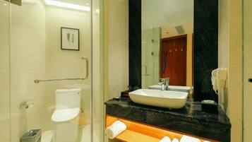 A modern bathroom with a glass shower enclosure, a white toilet, a large mirror, and a black marble countertop.