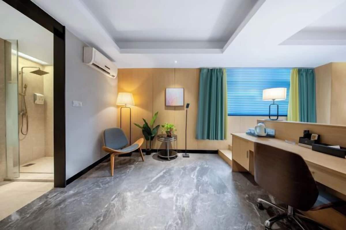 Une chambre d’hôtel moderne équipée d’une douche, d’un bureau, d’une chaise, d’une lampe et d’une fenêtre avec des rideaux.