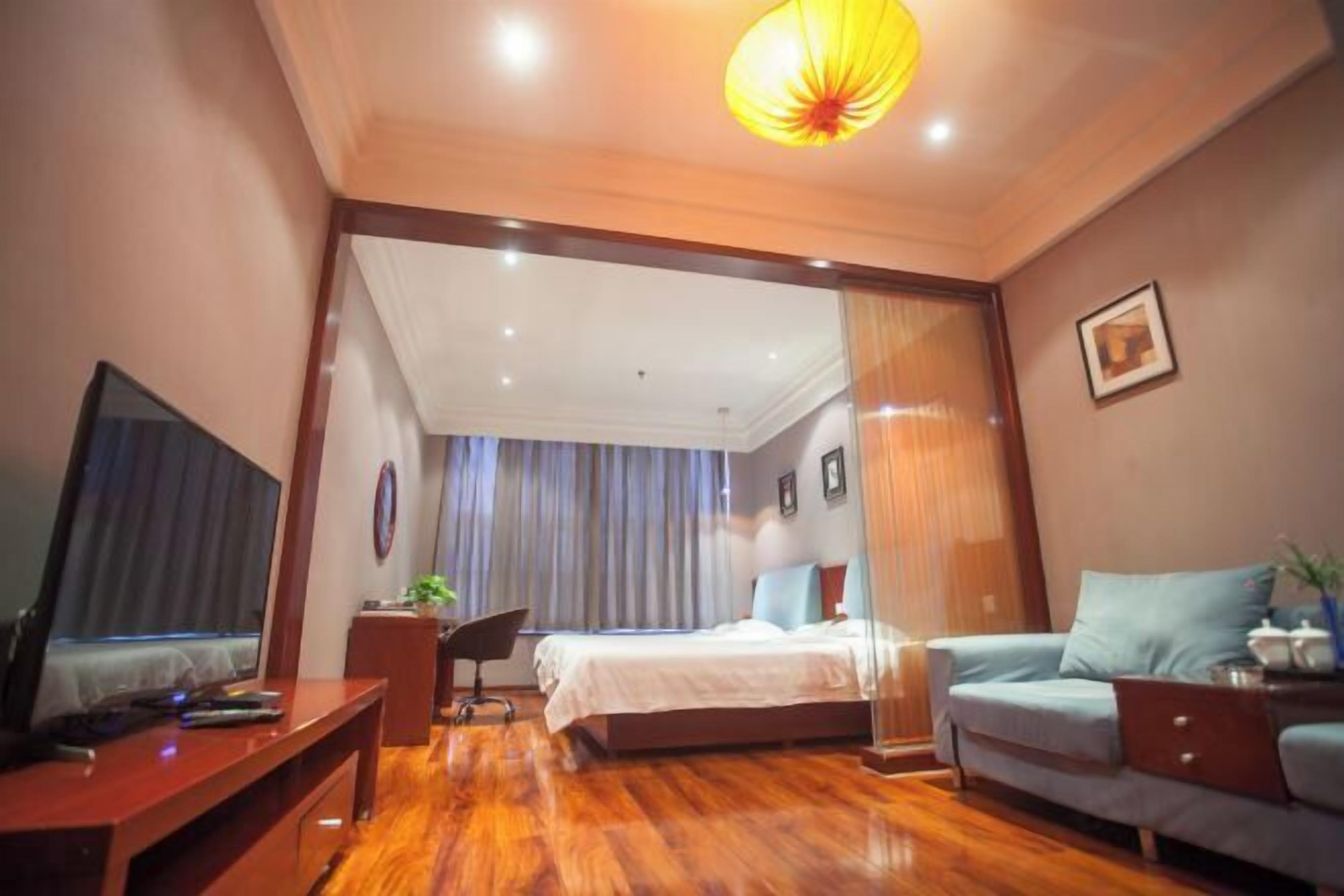 A hotel room with a wooden floor, a bed, a desk, a TV, and a sofa.