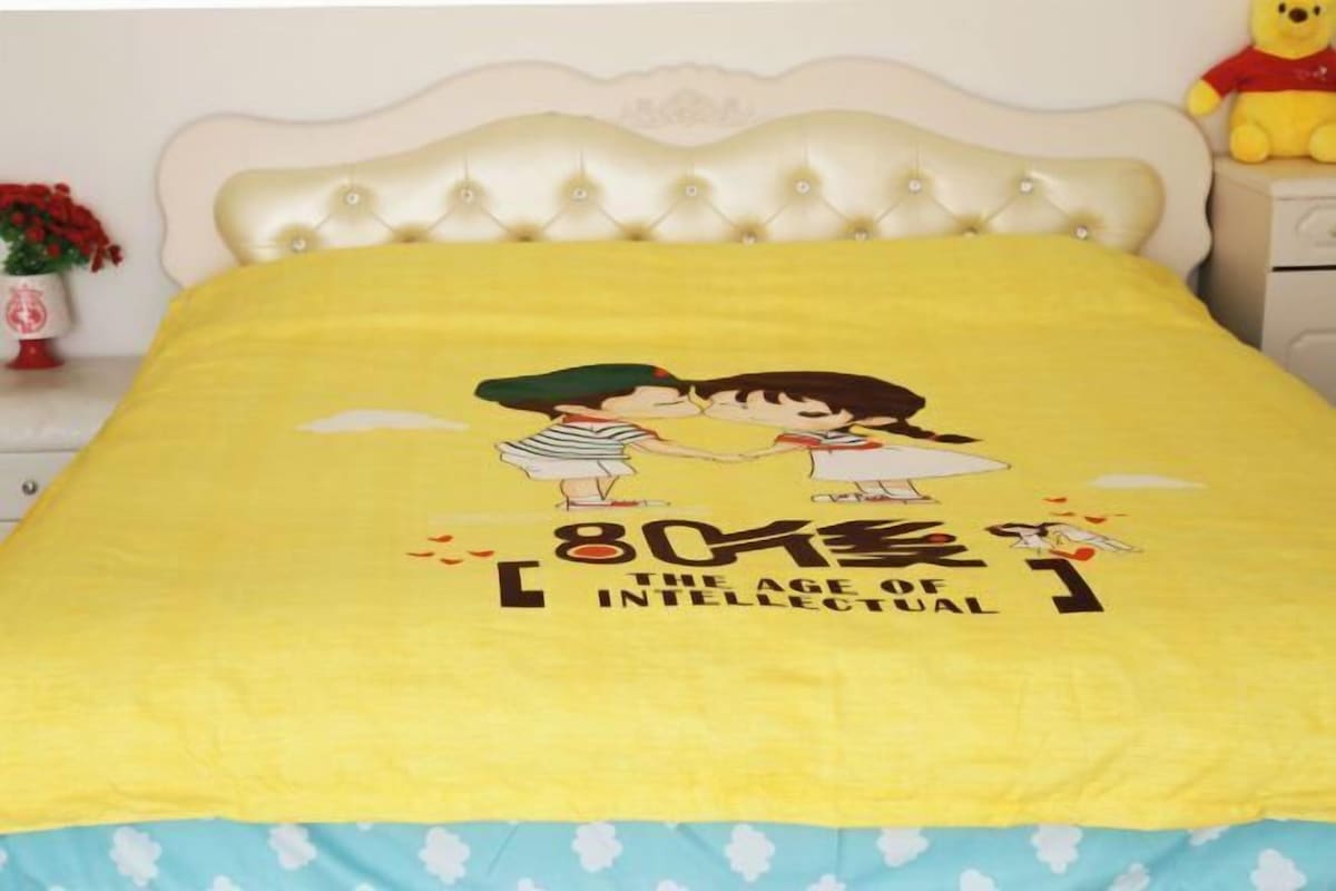 A bed with a yellow bedspread featuring a cartoon couple and the text "The Age of Intellectual."