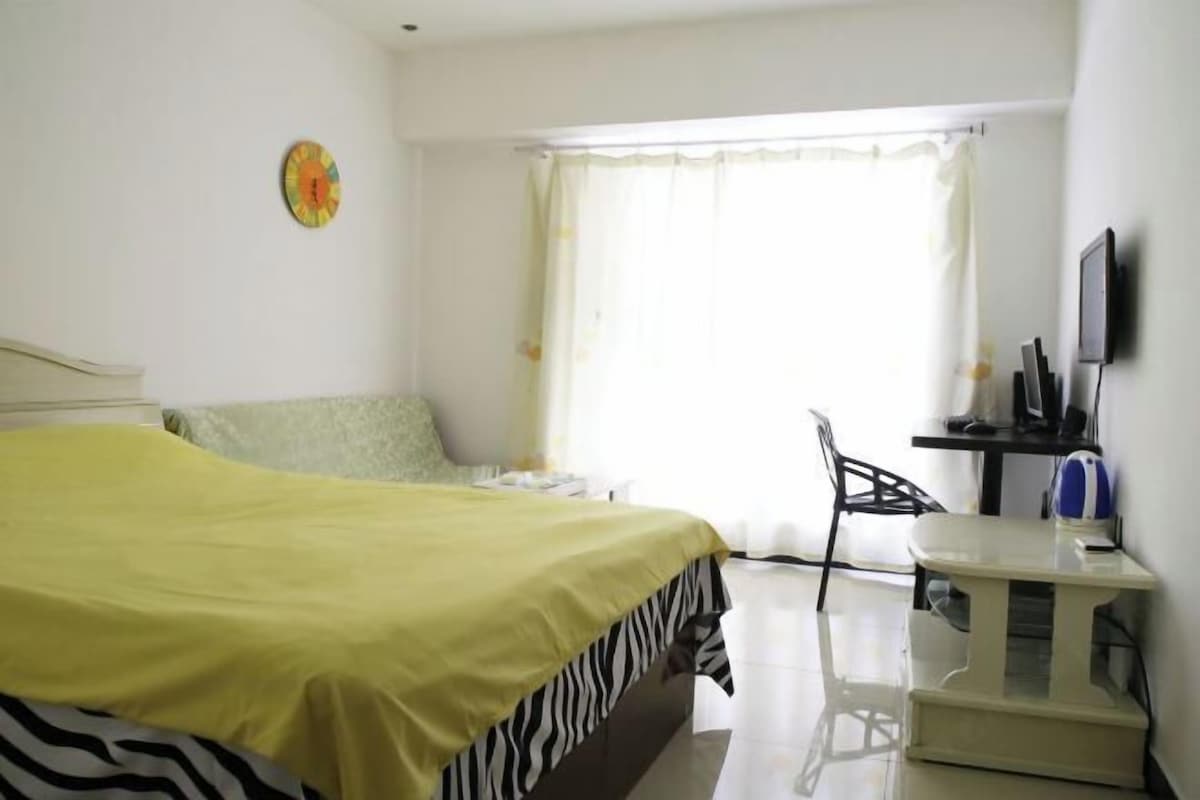 A bedroom with a bed, a desk, a chair, a television, and a window with curtains.