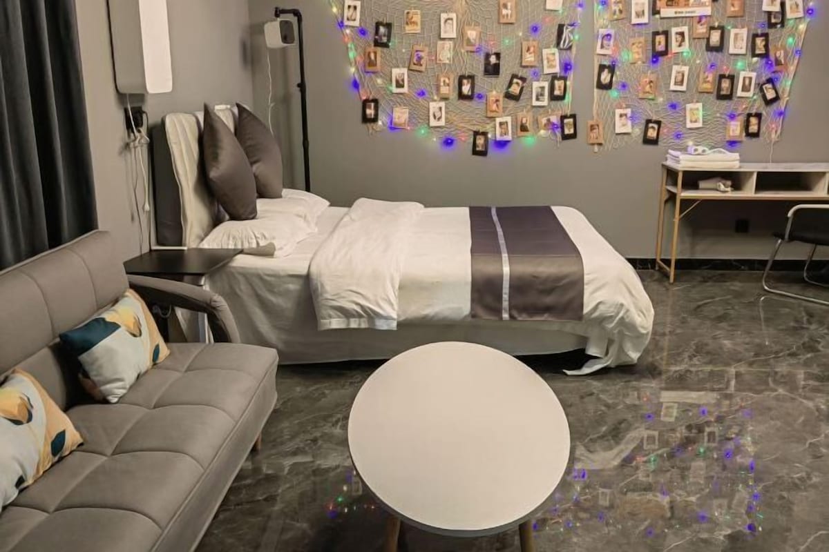 A modern hotel room with a bed, a round table, a sofa, and a wall decorated with photos.