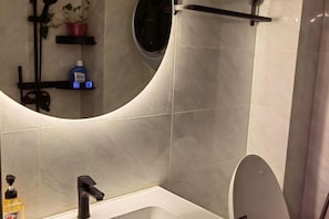 A modern bathroom with a white bathtub, a black faucet, a round mirror, and a shelf with toiletries. - Mizilan Zhengzhou Hotel (Guomao 360) (Zhengzhou)