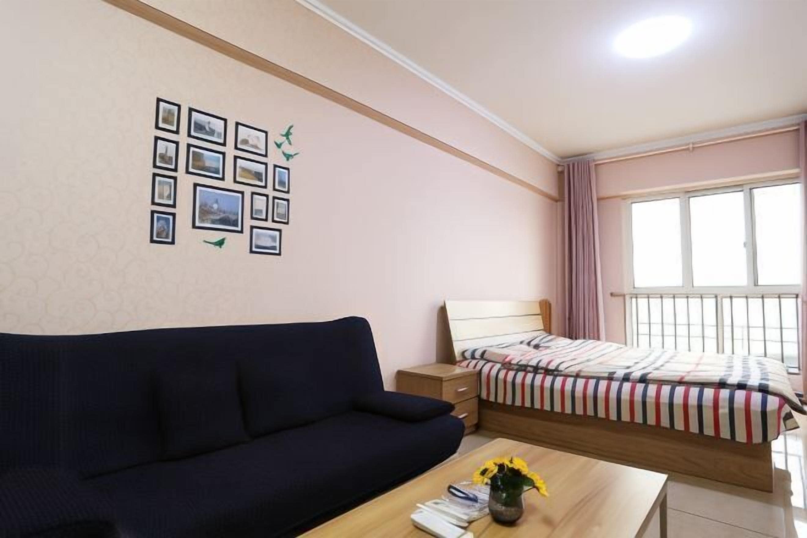 A bedroom with a bed, a sofa, a bedside table, a window with curtains, and a wall with framed pictures.
