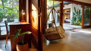Una habitación con un escritorio de madera, una silla colgante, una planta en maceta y vistas al exterior.
