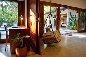 A room with a wooden desk, a hanging chair, a potted plant, and a view of the outdoors.