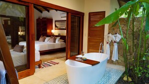 Un dormitorio con cama, un baño con bañera y vistas a un jardín.