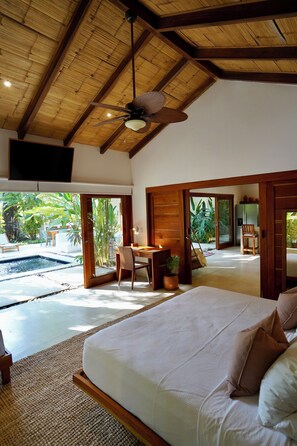 A bedroom with a bed, a desk, and a chair, a ceiling fan, and a view of an outdoor pool area.