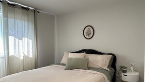 Ein Schlafzimmer mit einem Bett, einem Nachttisch, einer Lampe und einem an der Wand hängenden Bild.