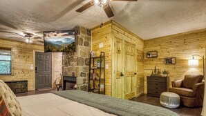 A cozy room with a bed, a stone fireplace, wooden walls, a bookshelf, and a chair.