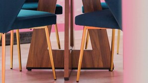 Een houten tafel met een bloempot, twee blauwe stoelen en een stapel boeken.