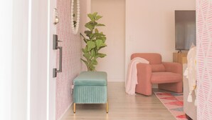 Een moderne, goed verlichte kamer met een houten vloer, een groene poef, een roze stoel en een televisie op een houten dressoir.