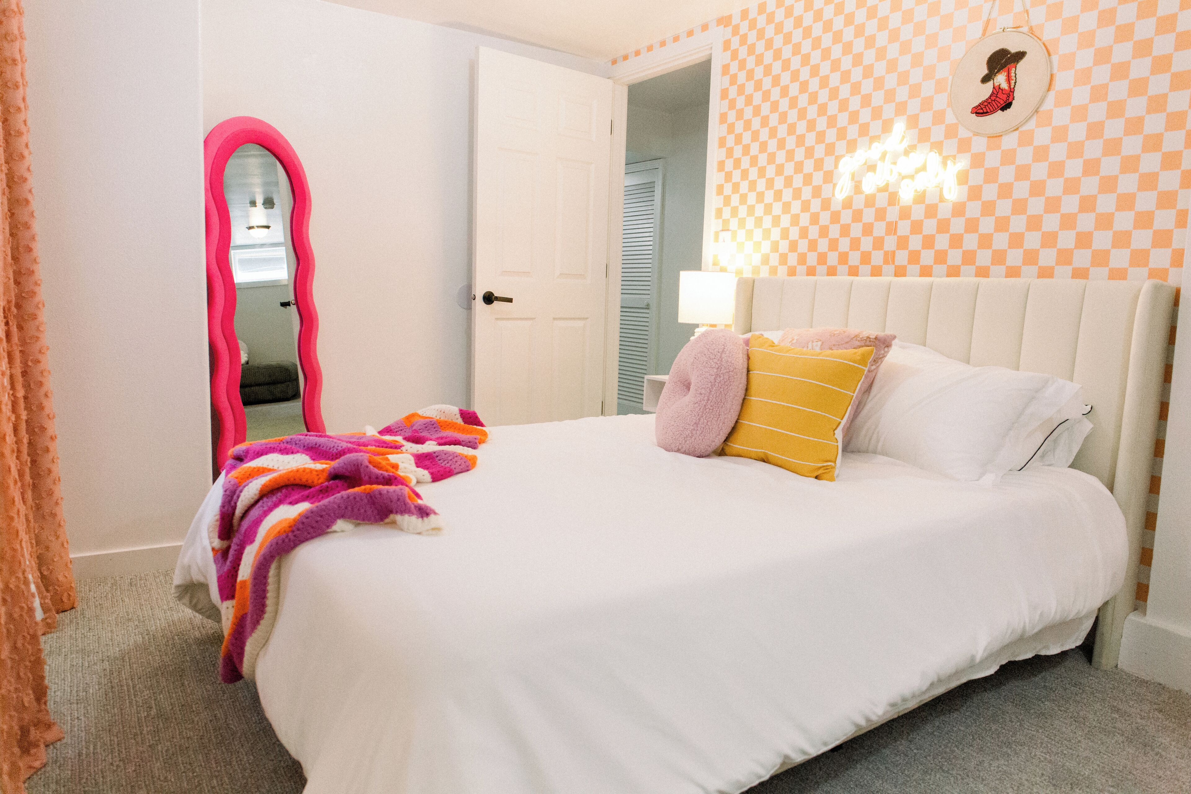 Une chambre avec un lit blanc, un miroir rose et un mur à carreaux.