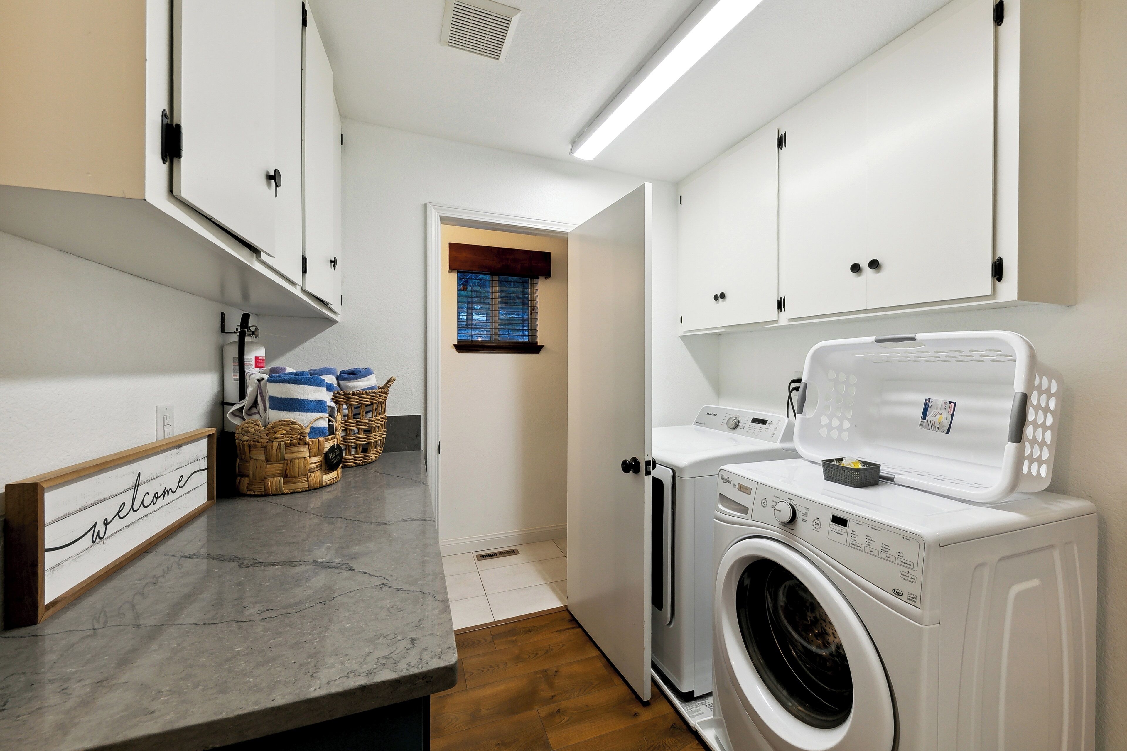 A laundry room with a washing machine, dryer, and a welcome sign on the wall.