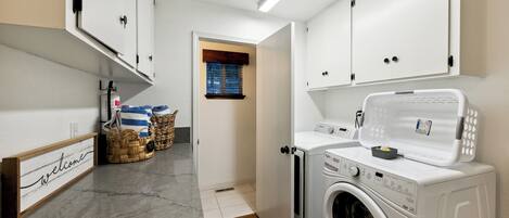 A laundry room with a washing machine, dryer, and a welcome sign on the wall.
