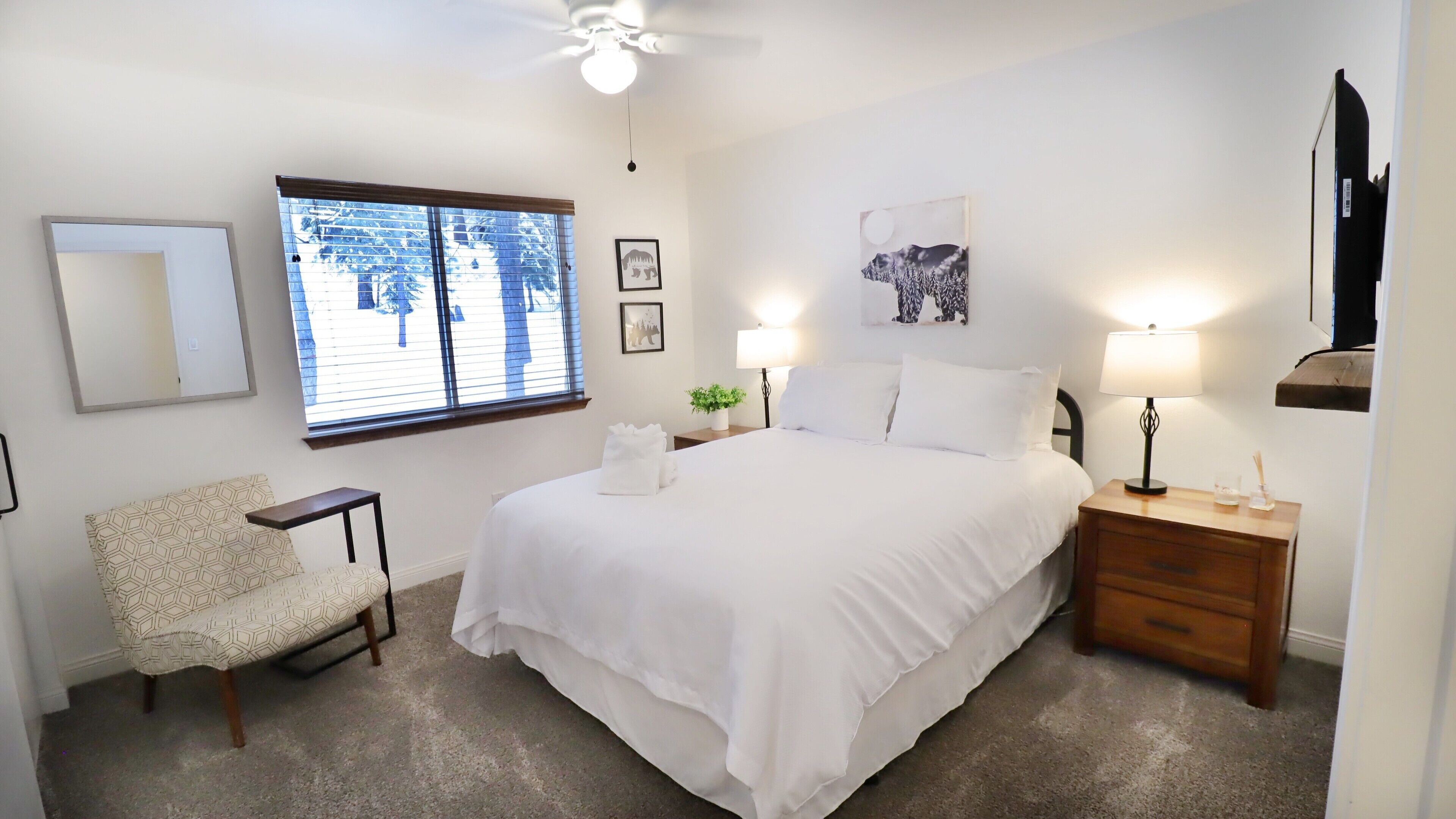 A neatly arranged bedroom with a bed, bedside tables, a chair, and a window with blinds.