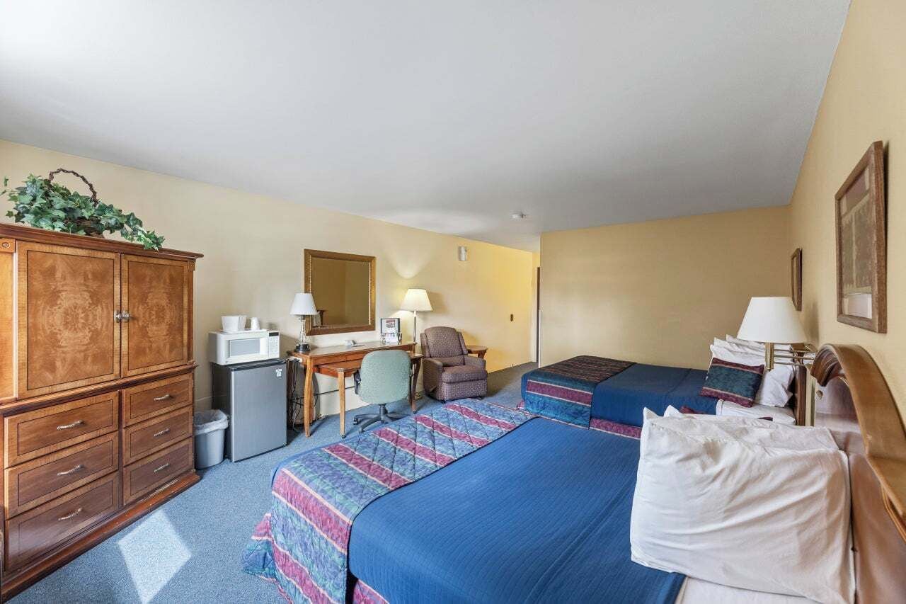 Une chambre d’hôtel avec deux lits, un bureau, une chaise, un petit réfrigérateur et un placard.