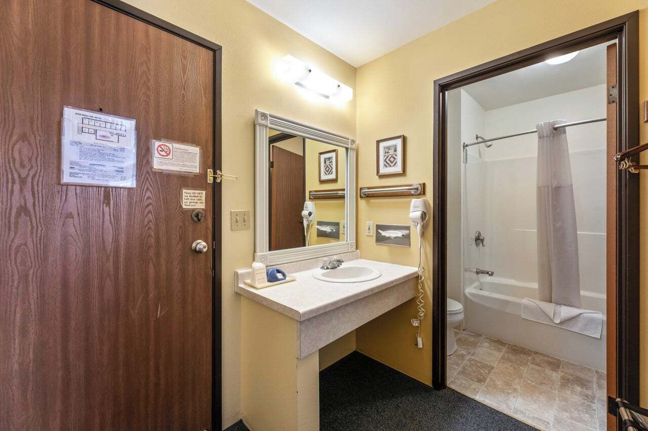 A hotel bathroom with a wooden door, a white sink with a mirror, a shower with a glass door, and a towel rack.