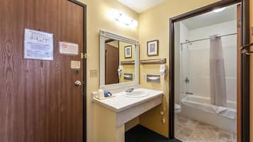 A hotel bathroom with a wooden door, a white sink with a mirror, a shower with a glass door, and a towel rack.