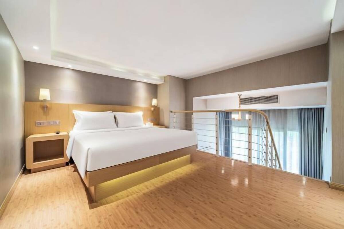 Une chambre d’hôtel moderne dotée d’un grand lit, d’une table de chevet, d’une commode, d’un bureau intégré et d’un escalier menant à un niveau supérieur.