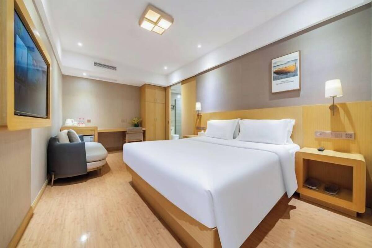 Une chambre d’hôtel avec un grand lit, un canapé, une table de chevet, une commode, une lampe fixée au mur et un tableau.