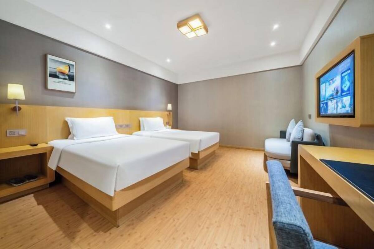 Une chambre d’hôtel avec deux lits, un bureau, une banquette et un téléviseur fixé au mur.