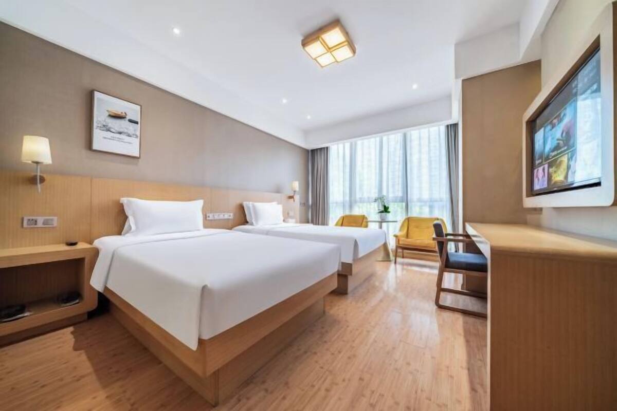 Une chambre d’hôtel avec deux lits, un bureau, une chaise, une télévision et une fenêtre.
