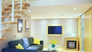 A modern living room with a sofa, a small table with a vase, a flat-screen TV mounted on the wall, and a fireplace. - Biz Boutique Hotel (Hangzhou)