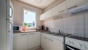 A modern kitchen with white cabinets, a built-in microwave, a stove, and a window providing natural light. - Le Filage - Balcon - Wifi (Laval)
