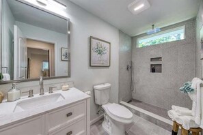 Ein modernes Badezimmer mit großem Spiegel, weißen Sanitärobjekten, einer Dusche und einem WC.
