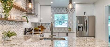 Una cocina moderna con encimeras de granito, electrodomésticos de acero inoxidable e iluminación colgante.