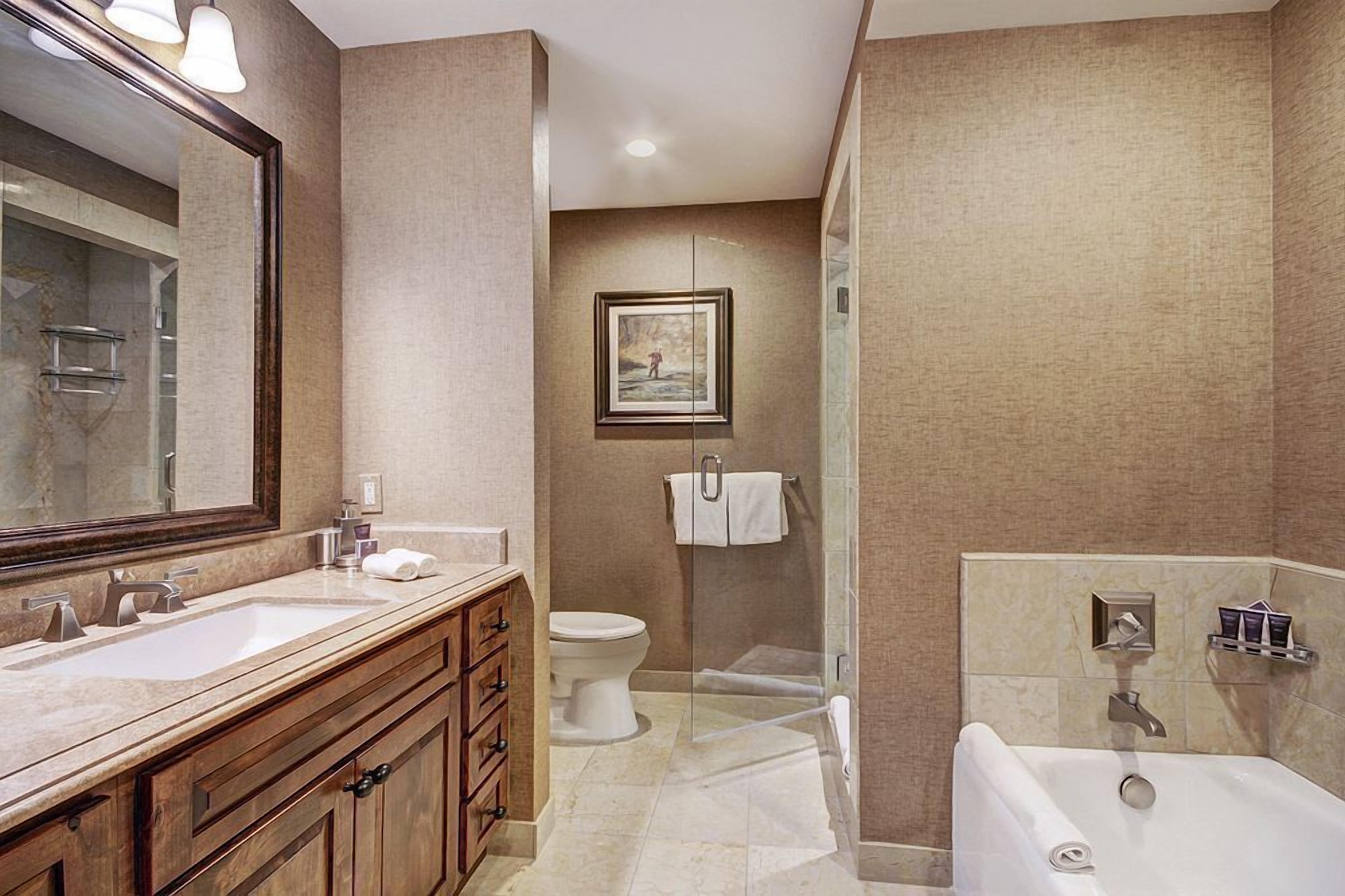 A modern bathroom with a large mirror, two sinks, a toilet, a shower, and a bathtub.