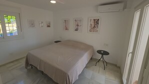 Un dormitorio con cama, ventilador de techo, una mesita y obras de arte colgadas en la pared.