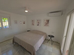 Un dormitorio con cama, ventilador de techo, una mesita y obras de arte colgadas en la pared.