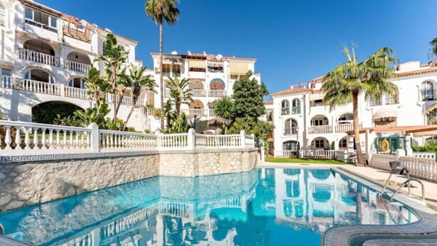 Una piscina con un muro de piedra, rodeada de edificios de varios pisos con balcones y palmeras.